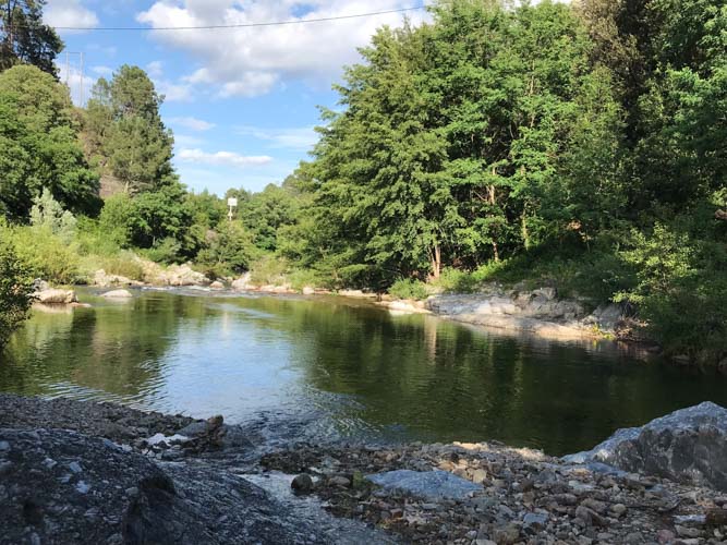 Rivière coulant le long du camping le petit baigneur entourée de verdure